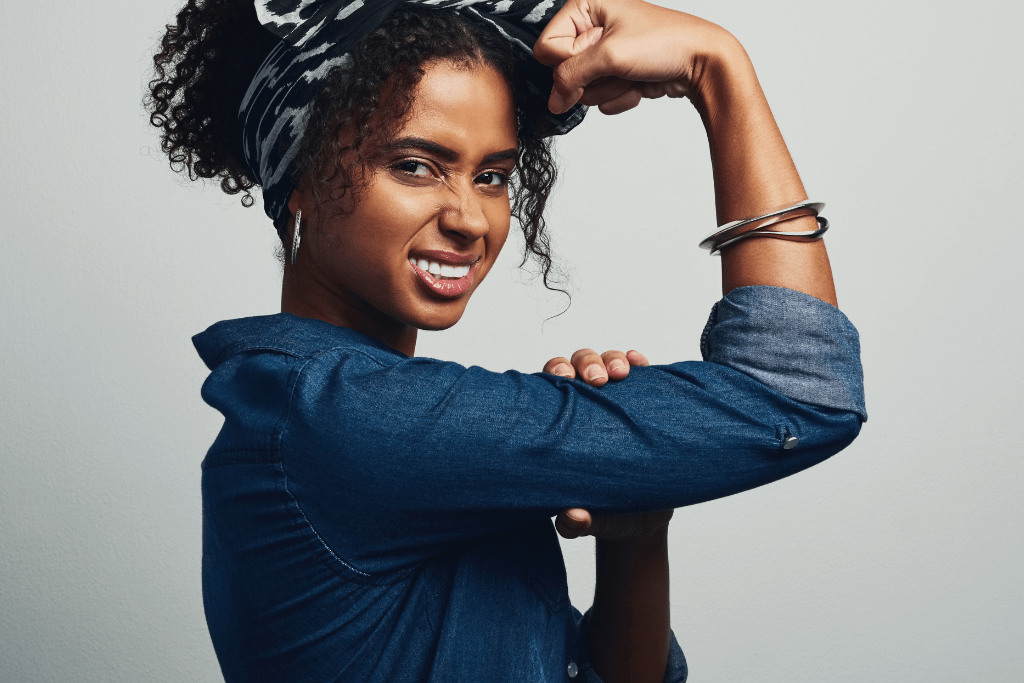 Studio shot of an attractive young woman posing against a grey background flexing her bicep