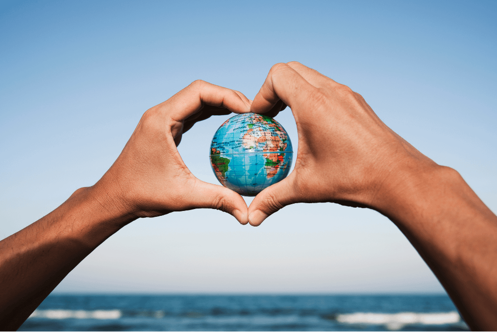 Man with a world globe in his hands forming a heart against the blue sky and beach in the background