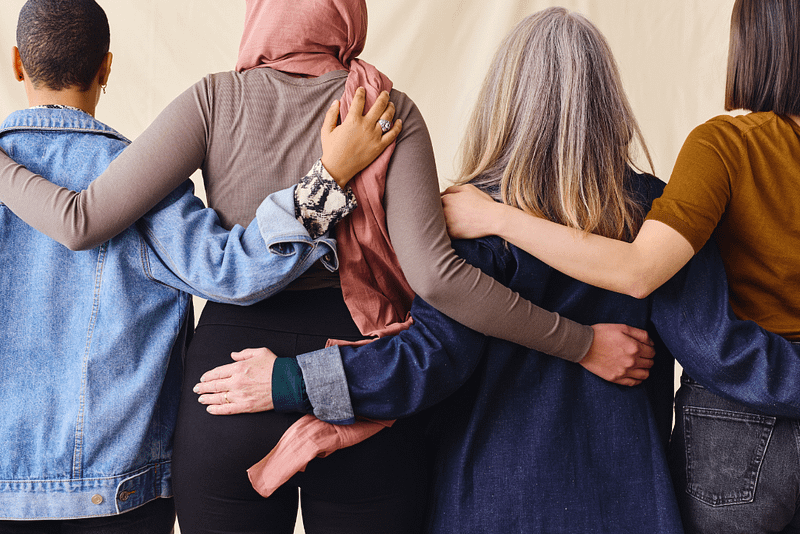 International Women's Day rear view portrait of four women standing with arms around each other in solidarity