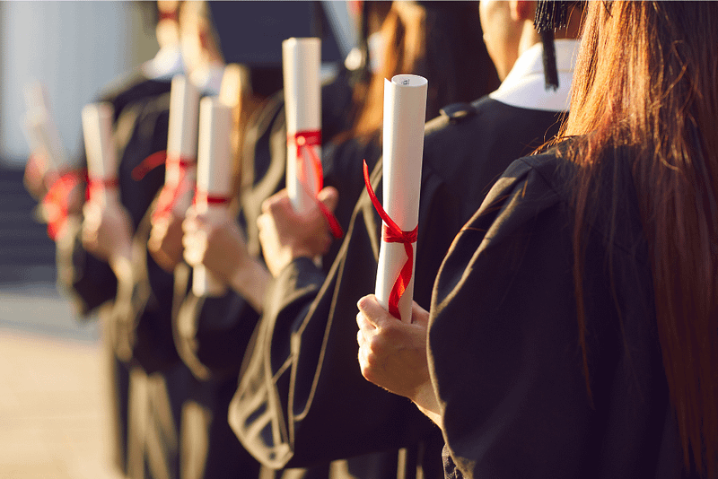 Graduates in black caps and gowns hold diplomas tied with red ribbons, symbolising achievement and success.